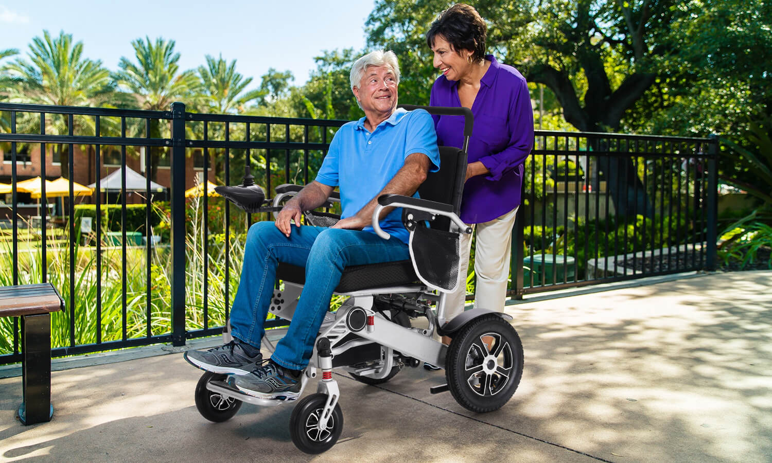 An_elderly_man_in_an_electric_wheelchair_with_a_woman_behind_him
